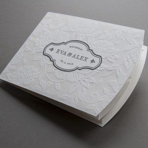 besondere faltbare Hochzeitseinladung im Letterpress bedruckt mit farblos geprägten floralen Elementen auf der Vorderseite der Klappkarte und den Namen des Brautpaares in Grau bedruckt.