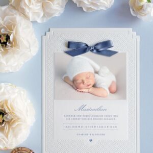 Letterpress Geburtskarte mit eleganter Prägung im A5 Format mit abgestuften Ecken, geprägtem Sternchenmuster und in Blau bedrucktem Text. Dazu ein aufgeklebtes Babyfoto, oberhalb eine blaue kleine Schleife in Blau