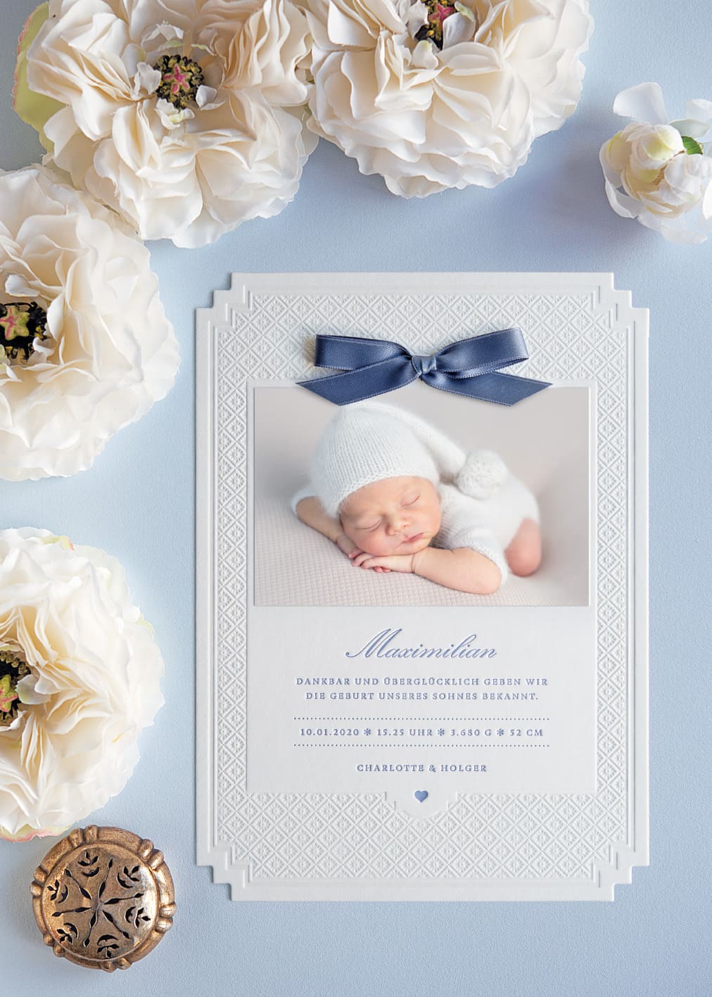 Letterpress Geburtskarte mit eleganter Prägung im A5 Format mit abgestuften Ecken, geprägtem Sternchenmuster und in Blau bedrucktem Text. Dazu ein aufgeklebtes Babyfoto, oberhalb eine blaue kleine Schleife in Blau