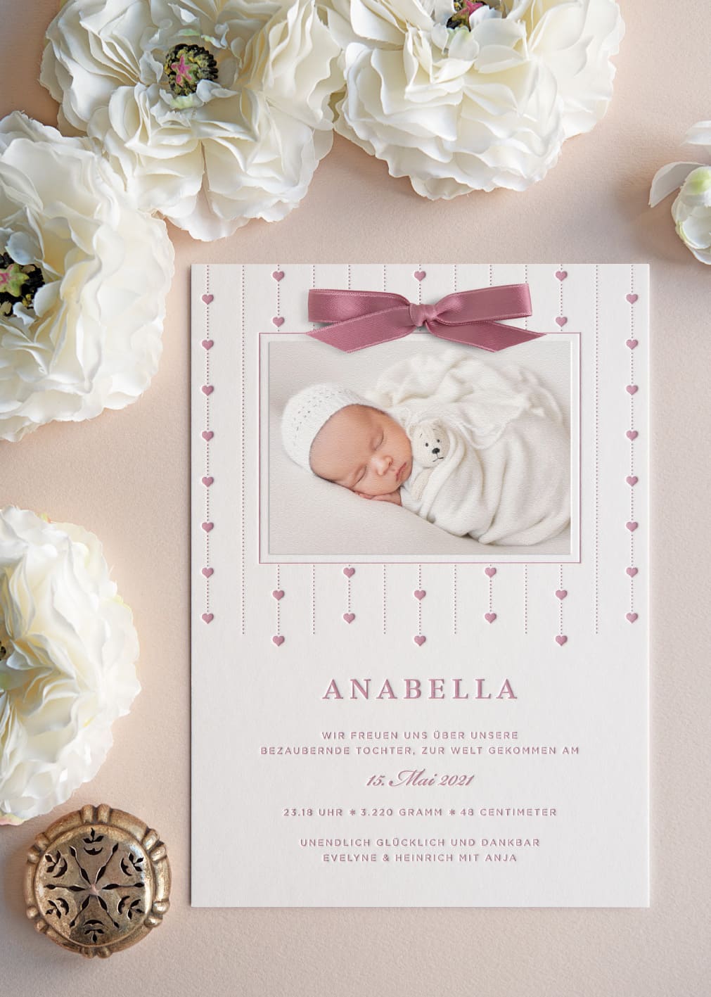 Eine Weiße Letterpress Geburtsanzeige für Maedchen, die mit wiederholenden pünktchen und Herzornamenten in Rosa rund um das Babyfoto bedruckt worden ist - es ist das Design B112