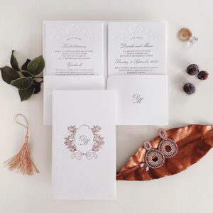 Hochzeitseinladung mit schmalen weißen Pockethülle und Hochzeitsmonogramm in Roségold geprägt